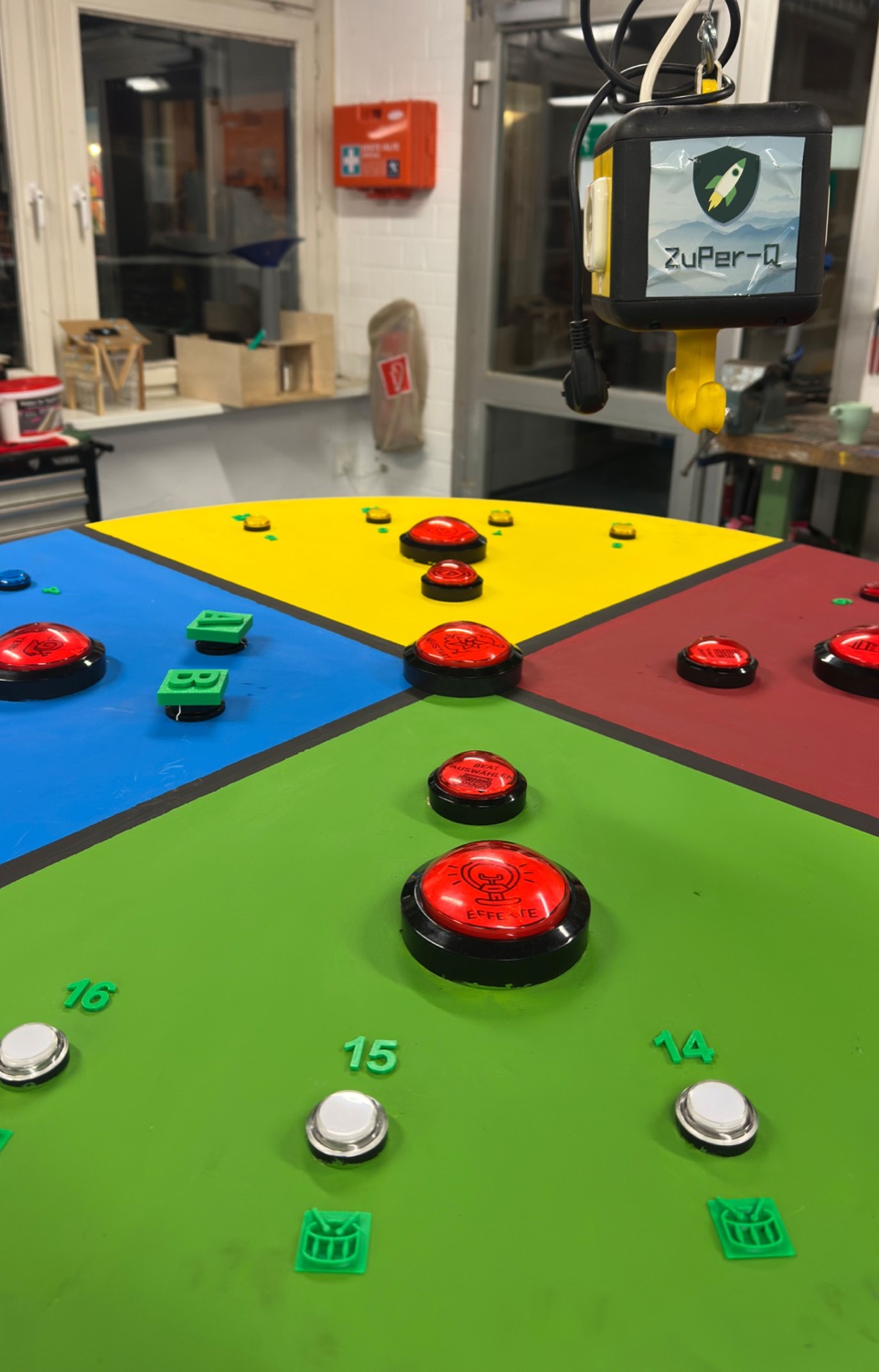 Round workshop table divided into four coloured quarters, with red and white arcade buttons