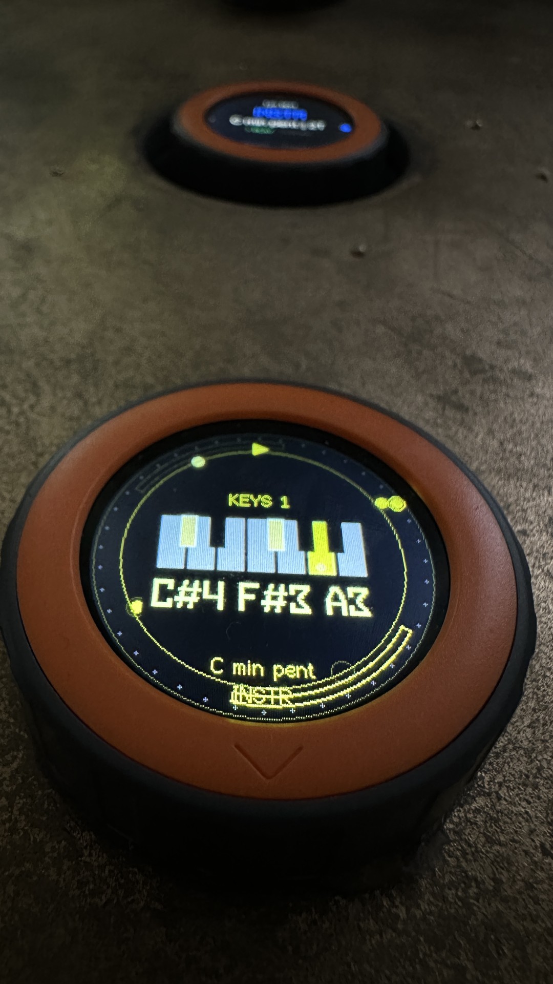 Close-up of a disc in yellow: the display shows KEYS 1, a keyboard, the note names C#4 F#3 A3, the scale C min pent and the mode INSTR; behind it a second disc, out of focus