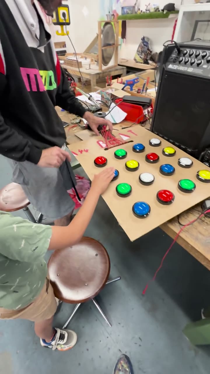 A teenager at a self-built cardboard beat machine with coloured buttons